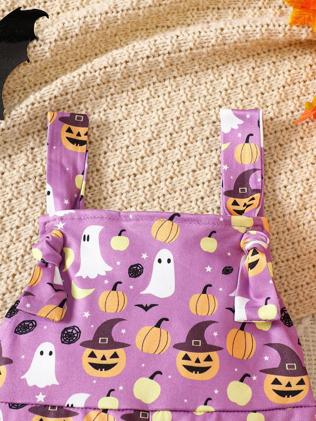 Close-up of the purple overalls' shoulder straps and Halloween-print bib.