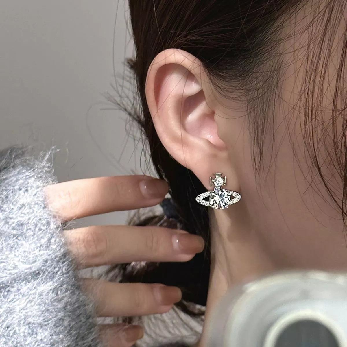 Silver-tone planet-shaped stud earrings with clear stones worn on a model
