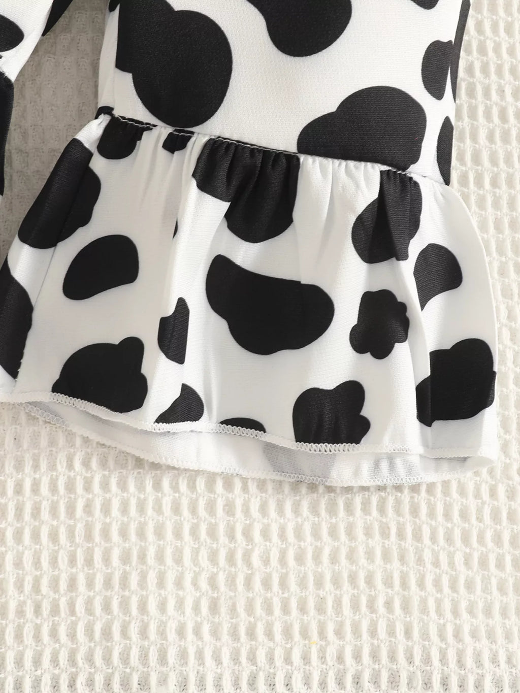 Close-up of the cow-print overalls' gathered waist seam.