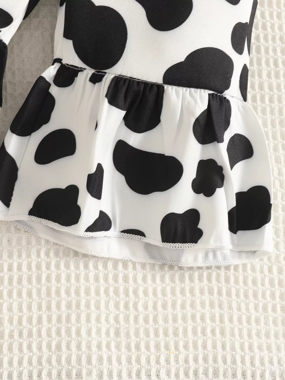 Close-up of the cow-print overalls' gathered waist seam.