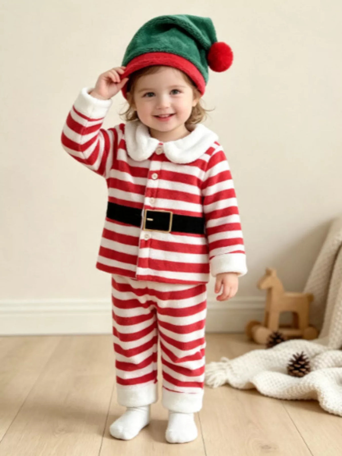 Red and white striped Christmas pajamas with printed black belt and green elf hat worn by a child