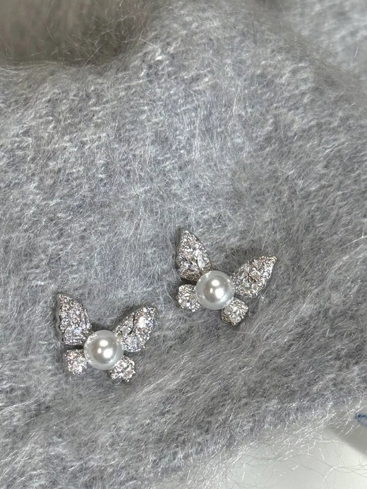 Butterfly-shaped pearl-like bead and clear stone stud earrings — detail view