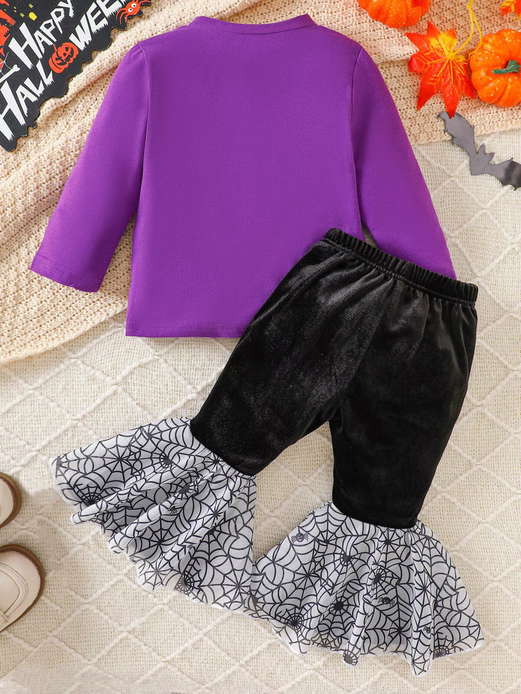 Back flat lay of the purple top and black pants with gray spiderweb flares.