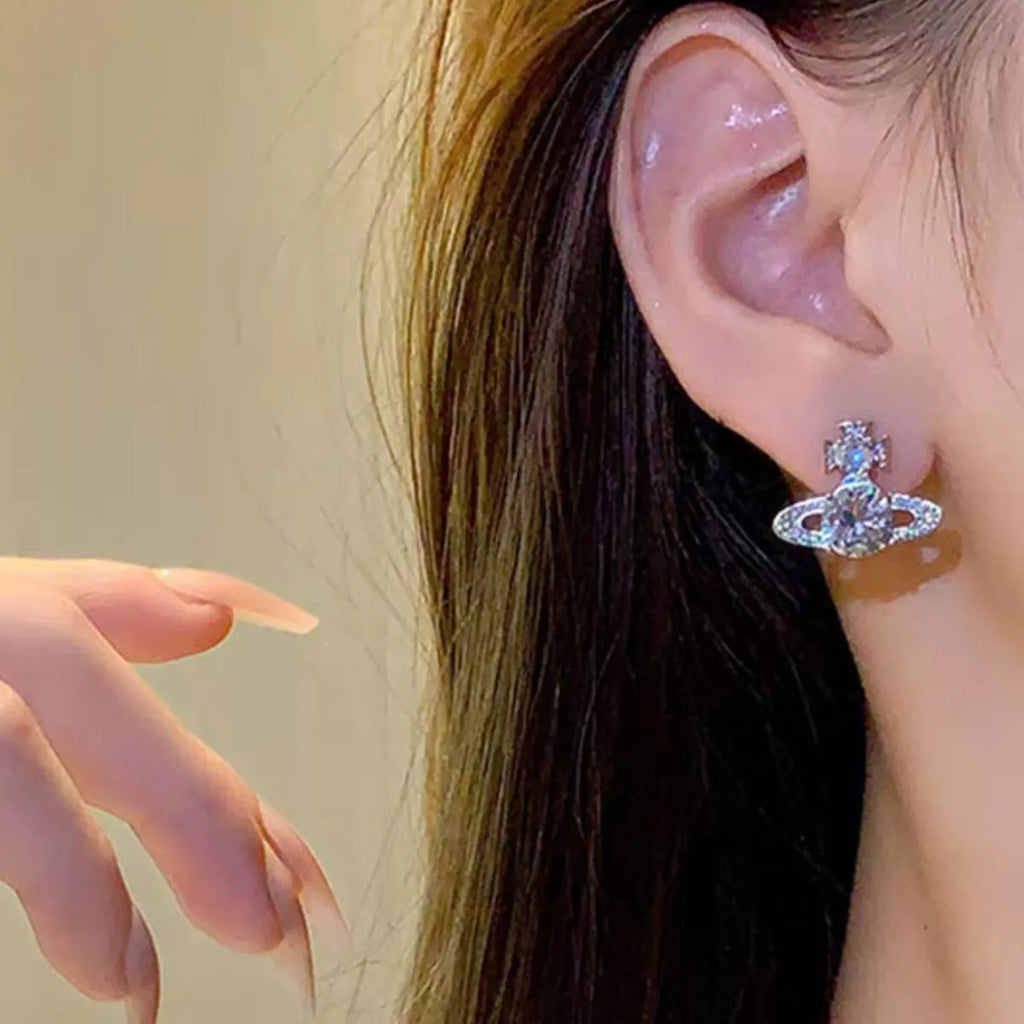 Silver-tone planet-shaped stud earrings with clear stones worn on a model