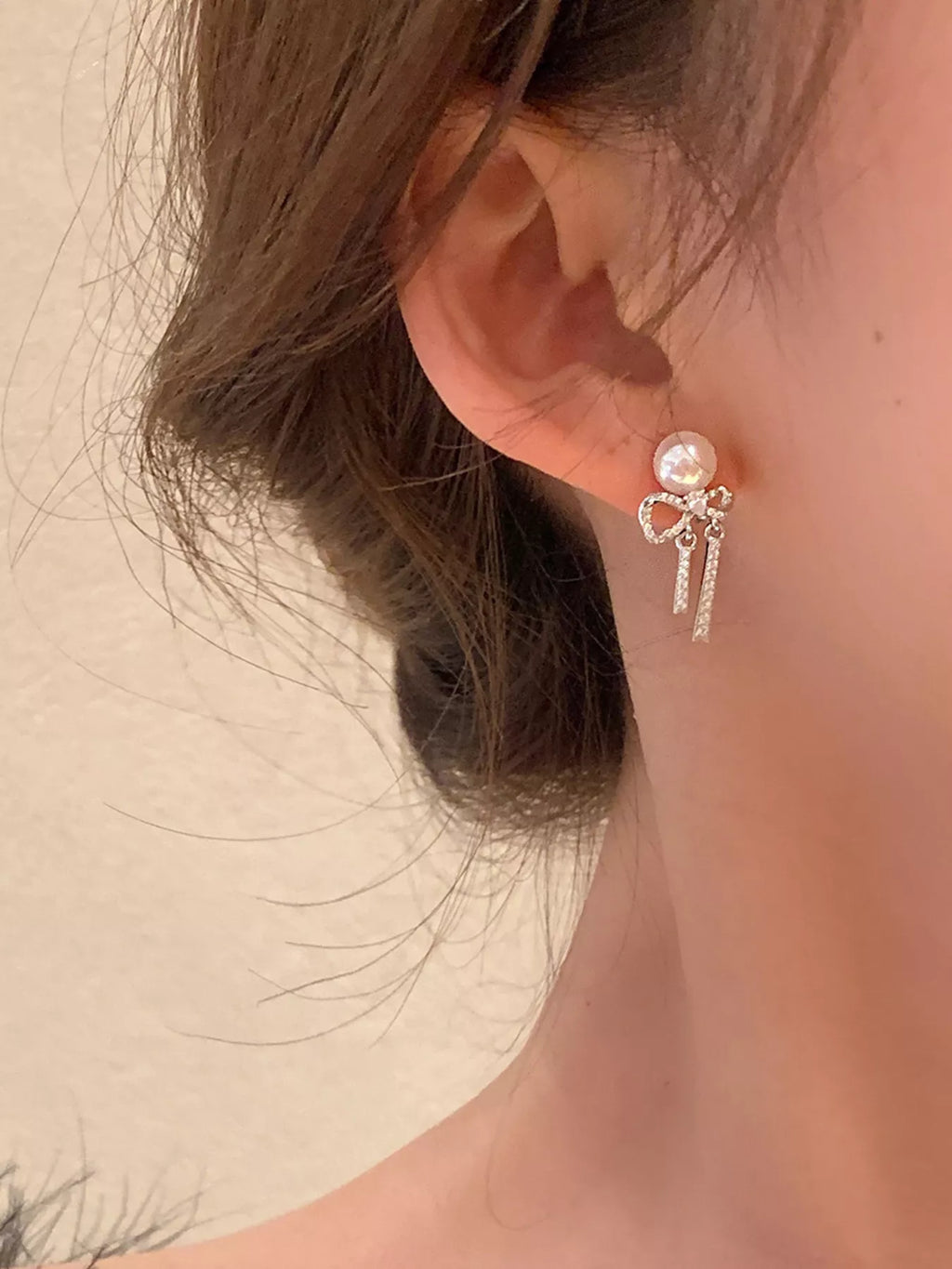 Bow-shaped drop earrings with pearl-like beads and chain tassels worn on a model