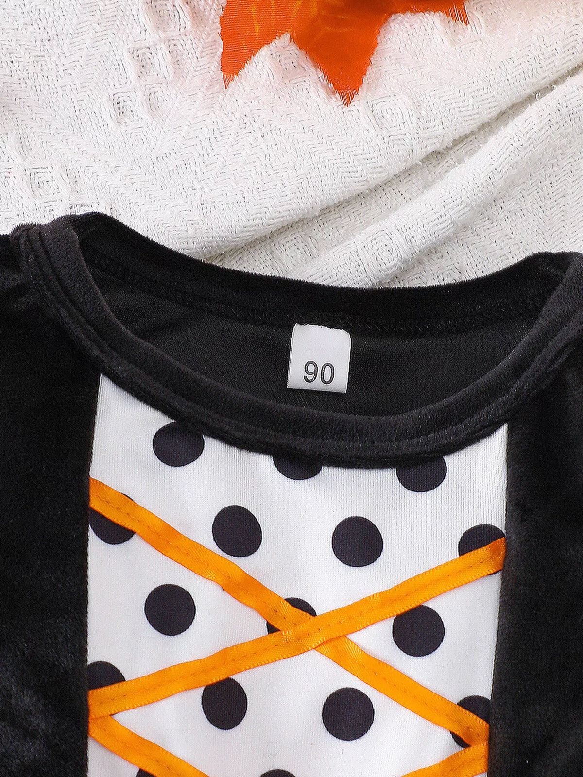 Close-up of the dress neckline and orange crisscross ribbons over white polka-dot fabric.