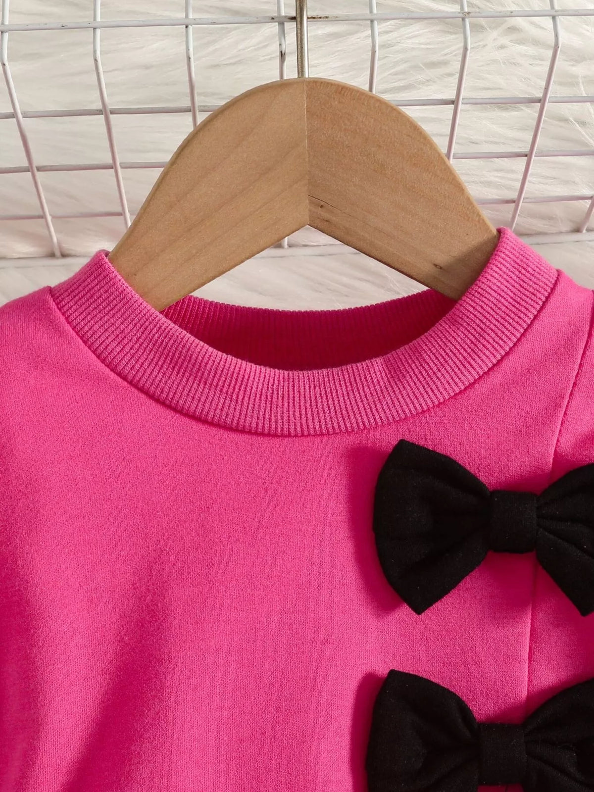 Close-up of the bright pink top's crew neckline and black bow applique.