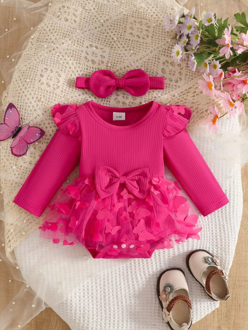Hot pink ribbed long-sleeve baby bodysuit with bow, ruffle trim and matching headband displayed flat