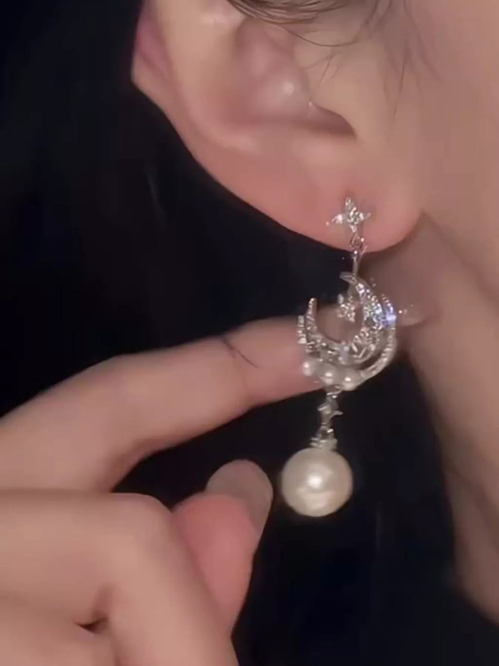 Moon and star dangle earrings with pearl-like bead drops worn on a model