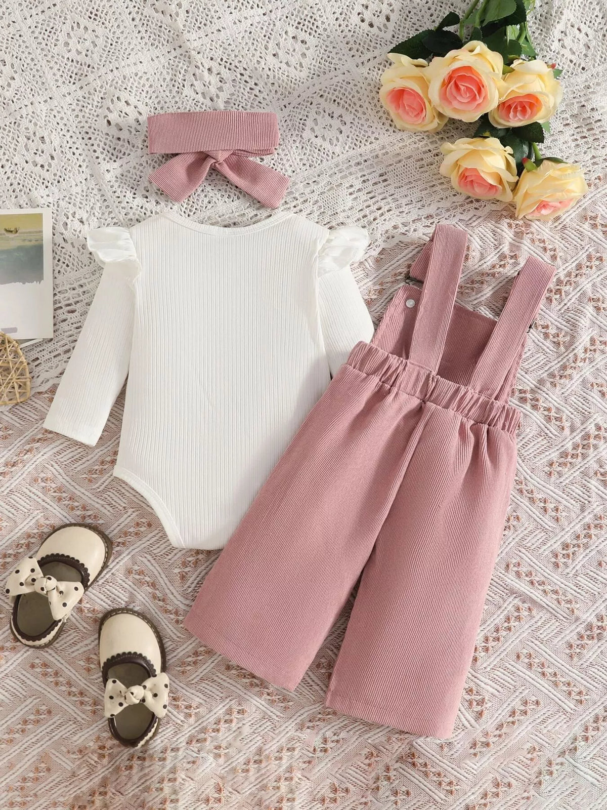 White ribbed baby bodysuit with pink bow-embroidered overalls and matching headband displayed flat