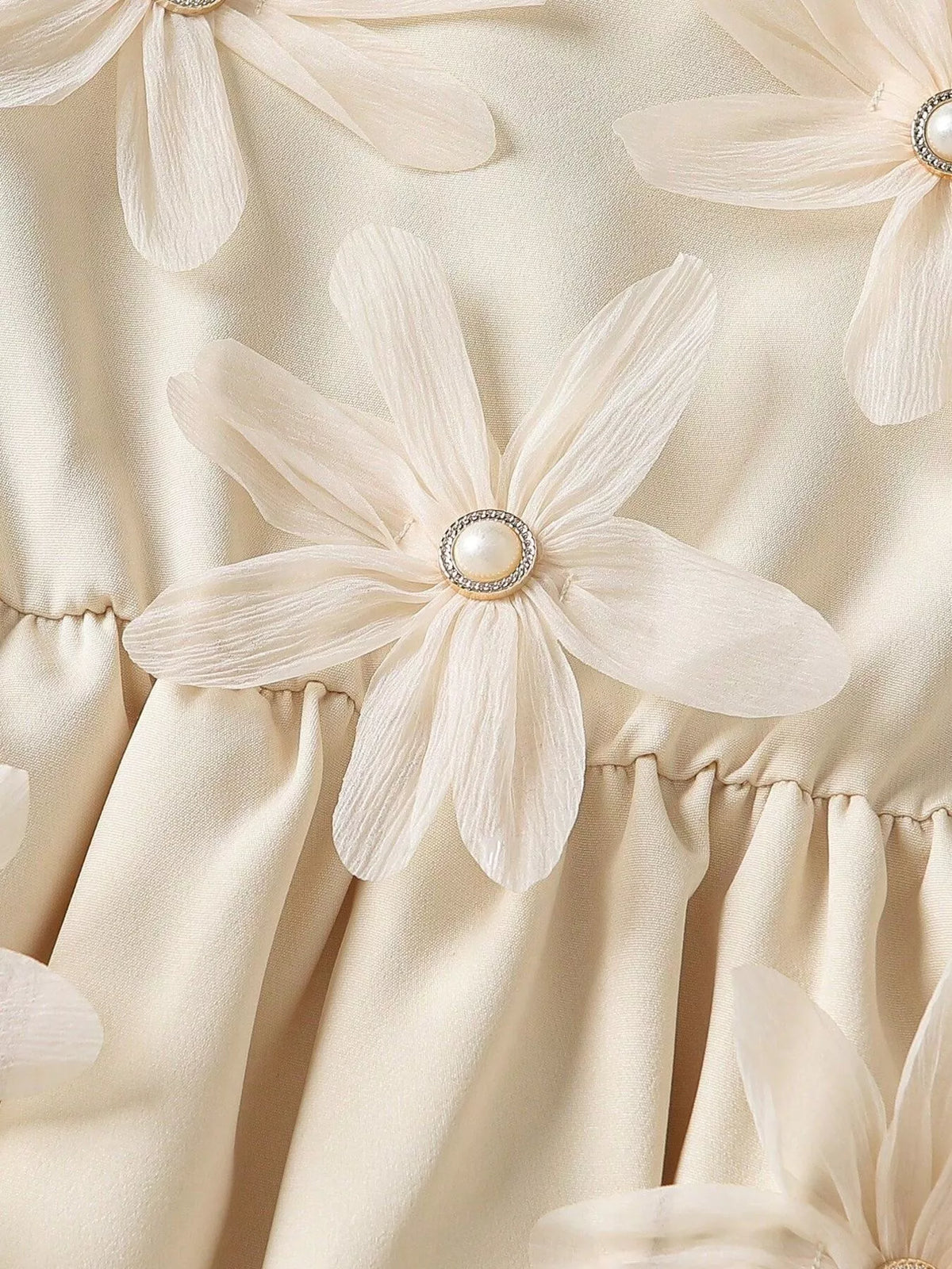 Close-up of a sheer-petal flower applique with pearl-look center on the cream dress.