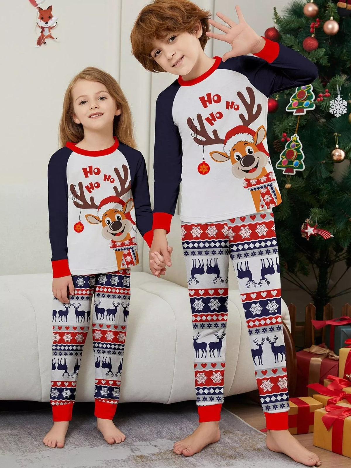 Two children wearing matching reindeer Christmas tops with navy sleeves and festive striped pants.