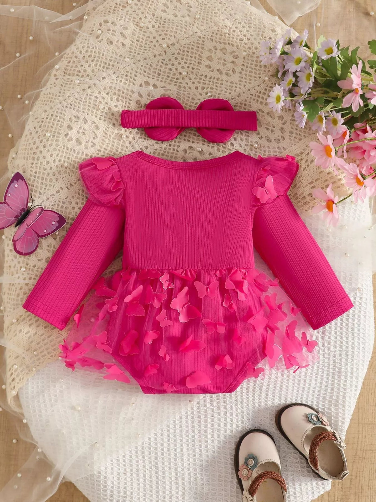 Hot pink ribbed long-sleeve baby bodysuit with bow, ruffle trim and matching headband displayed flat