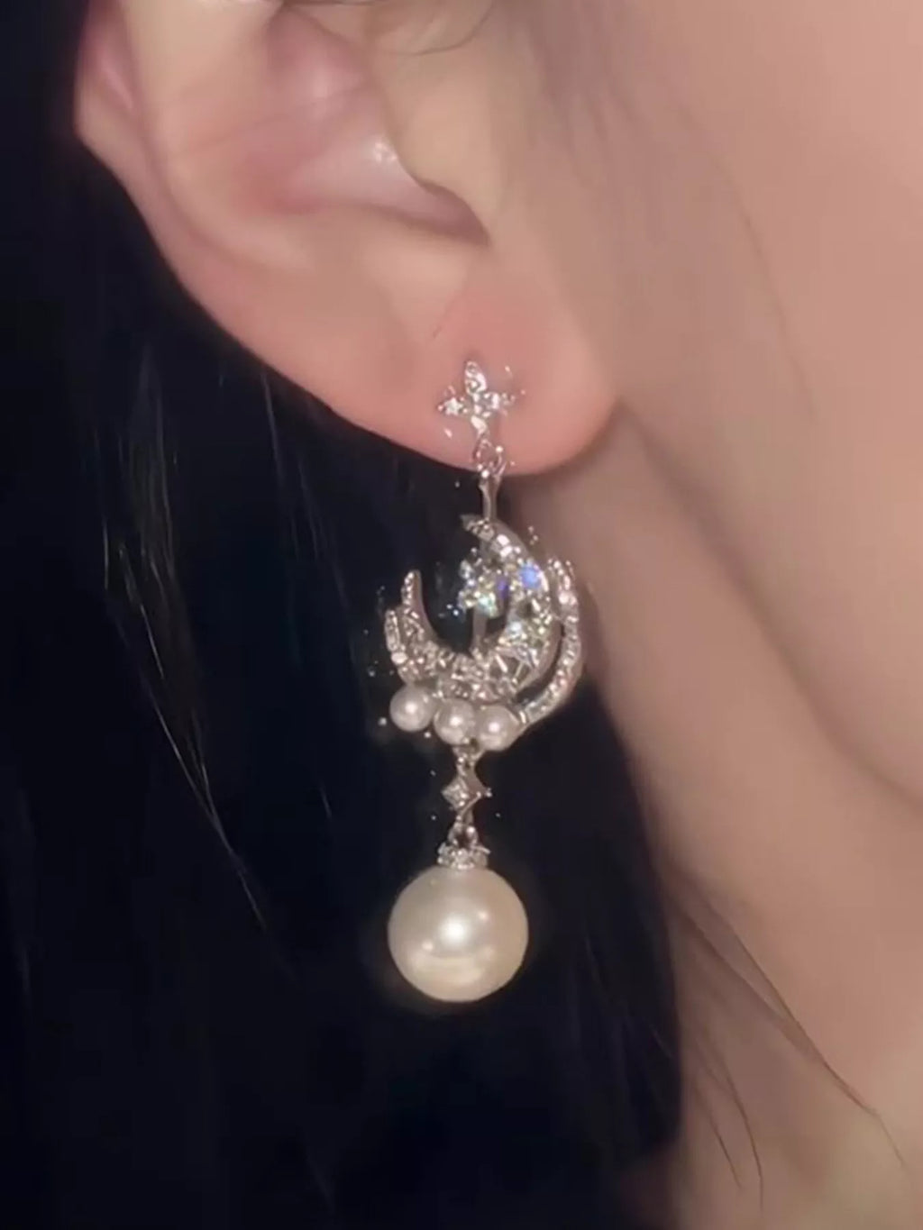Moon and star dangle earrings with pearl-like bead drops worn on a model