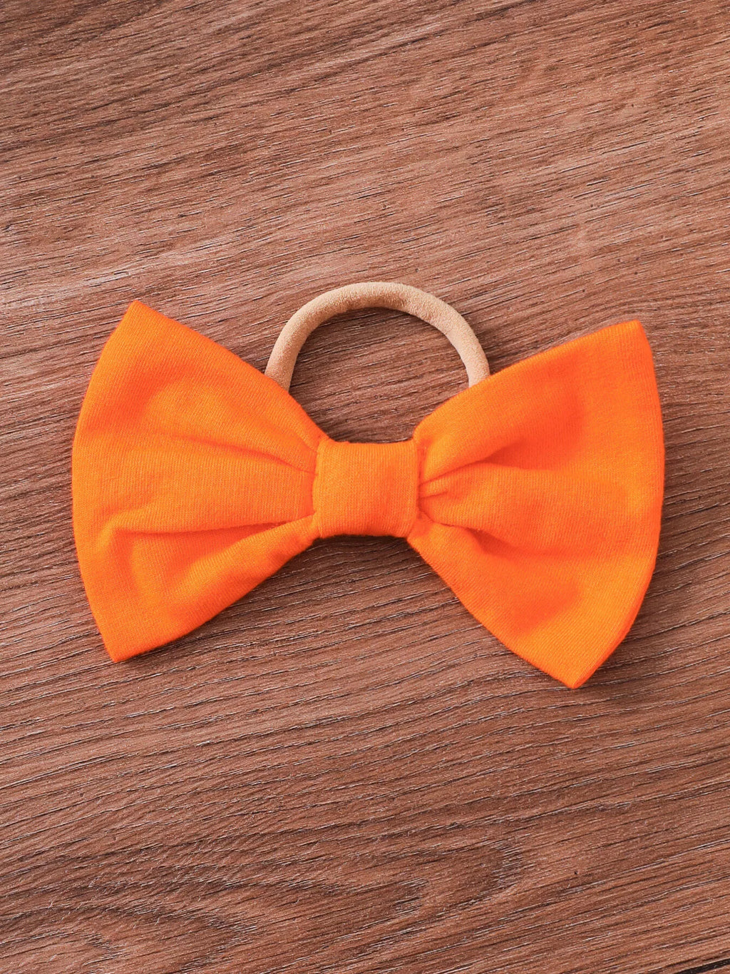 Orange baby bow headband on a wooden surface.