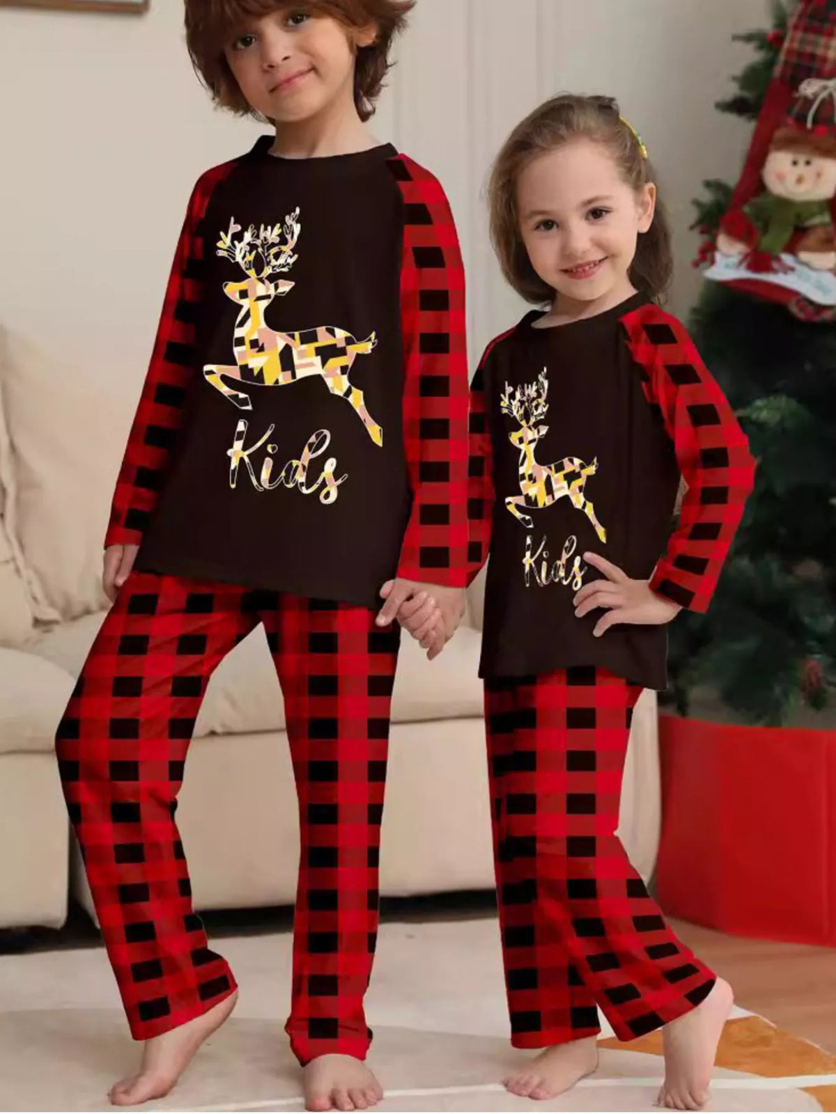 Two children wearing matching black reindeer graphic tops and red plaid pajamas.