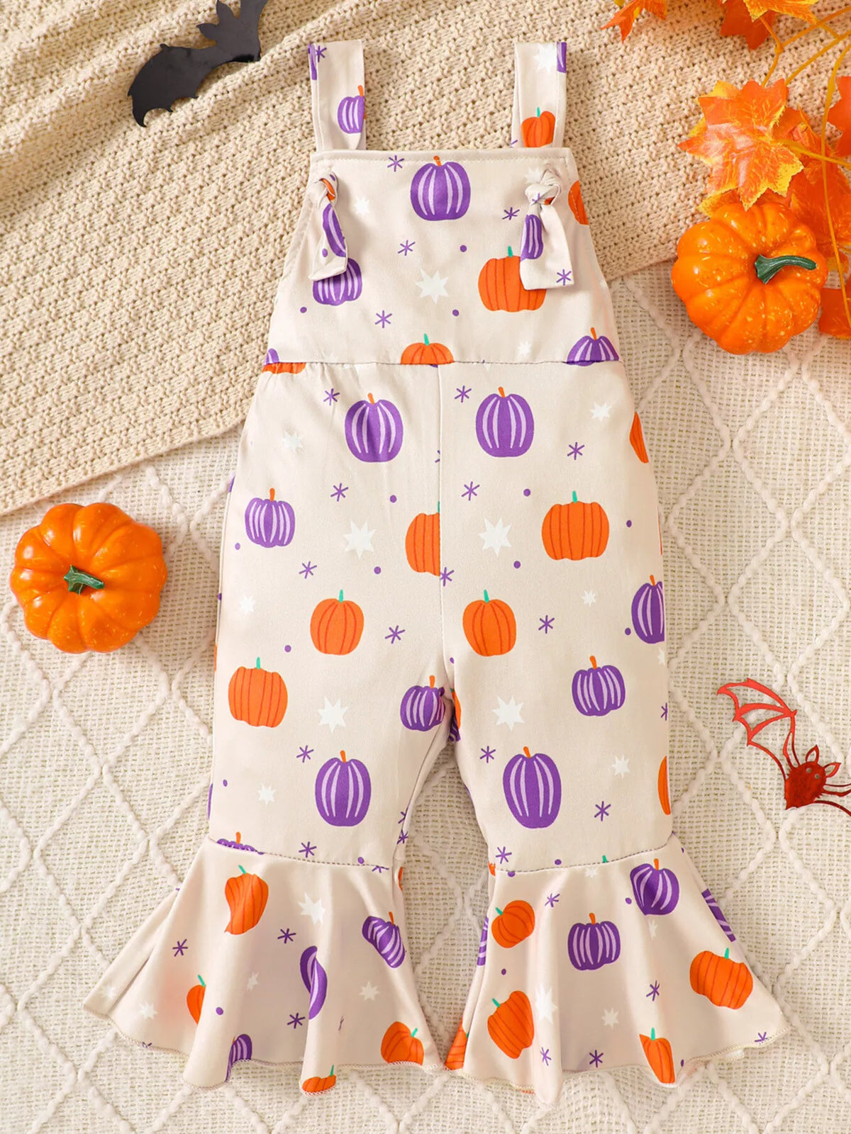 Cream suspender overalls printed with orange and purple pumpkins and stars.