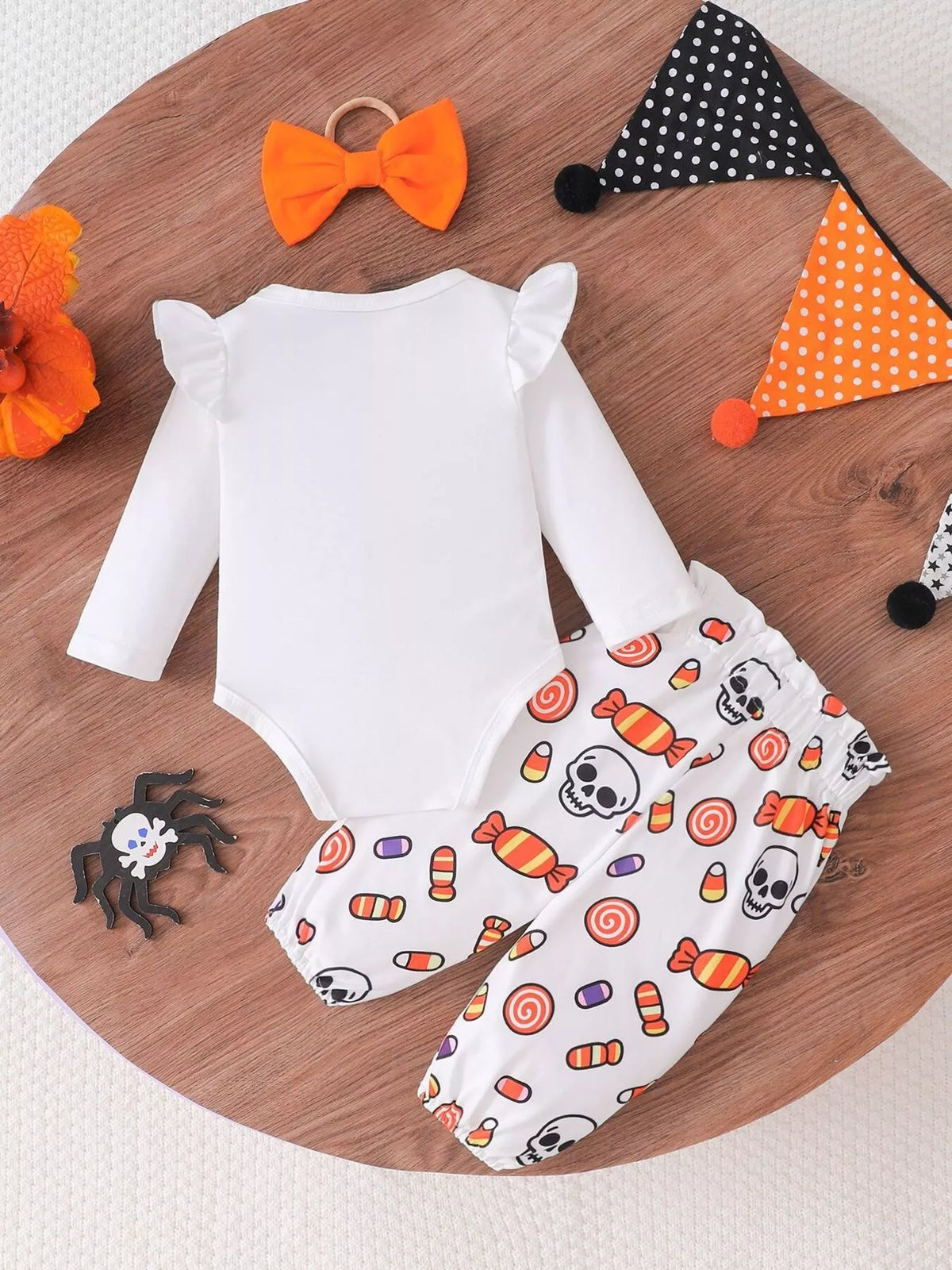Back flat lay of the white bodysuit, Halloween candy-print pants and orange bow headband.