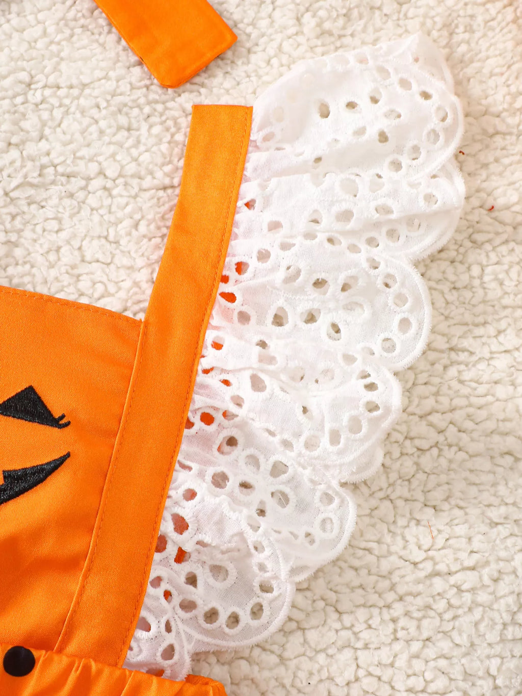 Close-up of the pumpkin romper's white eyelet shoulder ruffles and orange straps.