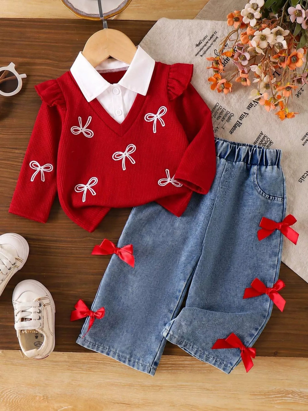 Children’s red bow-embellished sweater with white collar and blue jeans with red bows displayed flat