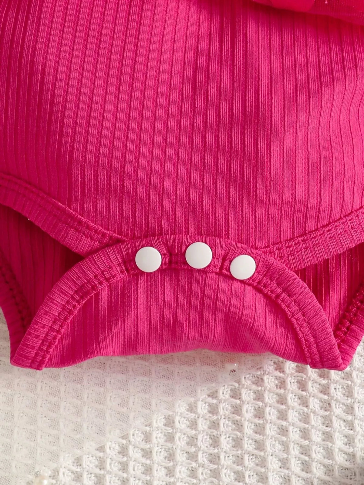 Snap fasteners and ribbed fabric on the hot pink baby bodysuit