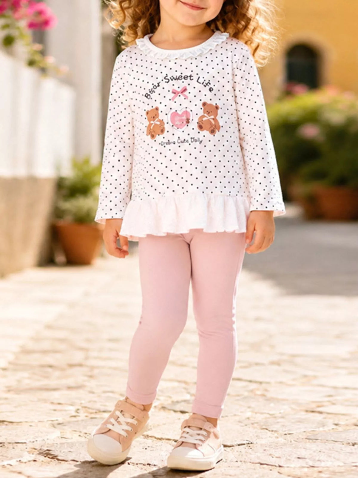 Children’s white polka-dot bear graphic ruffle-hem top with pink leggings worn by a child