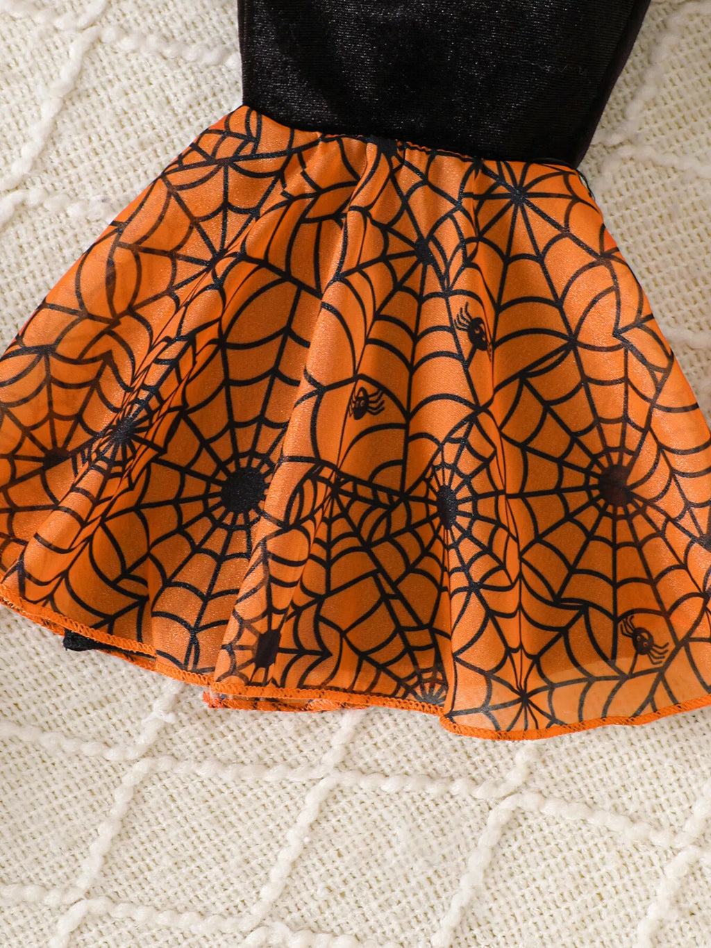 Close-up of the orange spiderweb-print flared hem on the black pants.