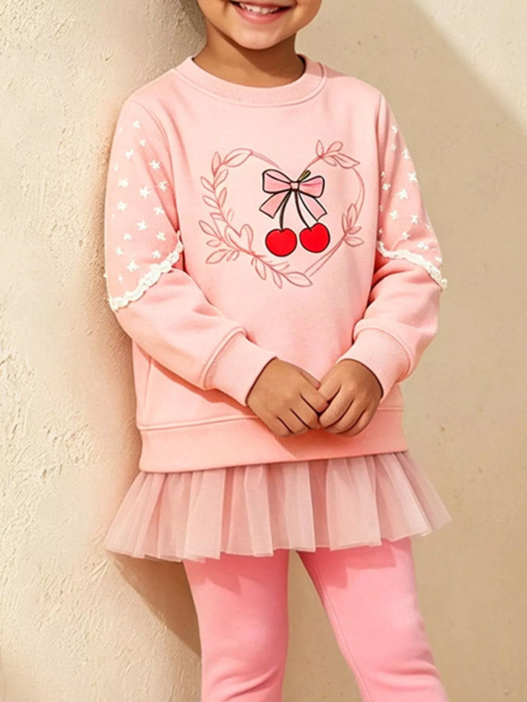 Close view of the cherry-and-bow graphic and tulle hem on a child's pink sweatshirt set.