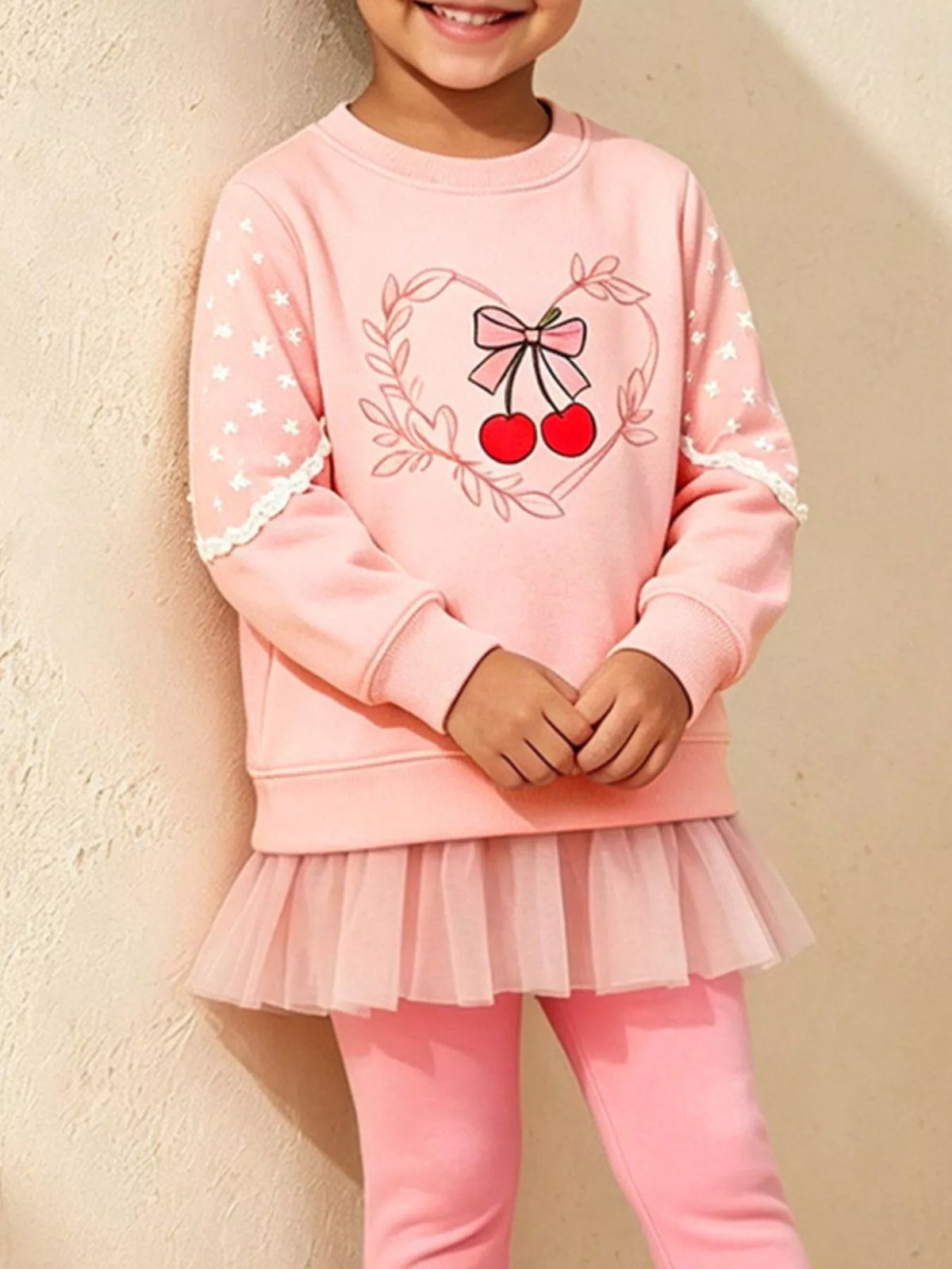 Close view of the cherry-and-bow graphic and tulle hem on a child's pink sweatshirt set.