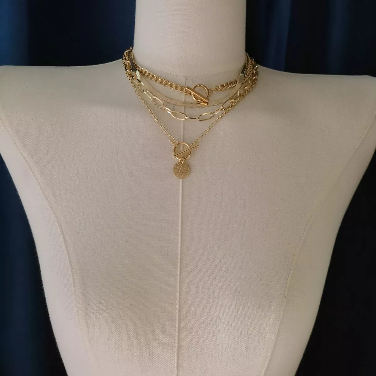 Four layered gold-tone necklaces with coin pendant and mixed chain styles