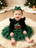 Baby wearing a black My 1st Christmas top, green plaid tulle skirt and green bow headband.