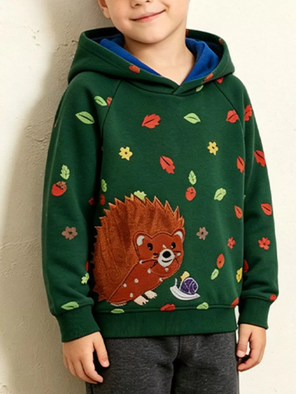 Children’s green hedgehog-print hoodie with contrasting blue hood lining worn by a child