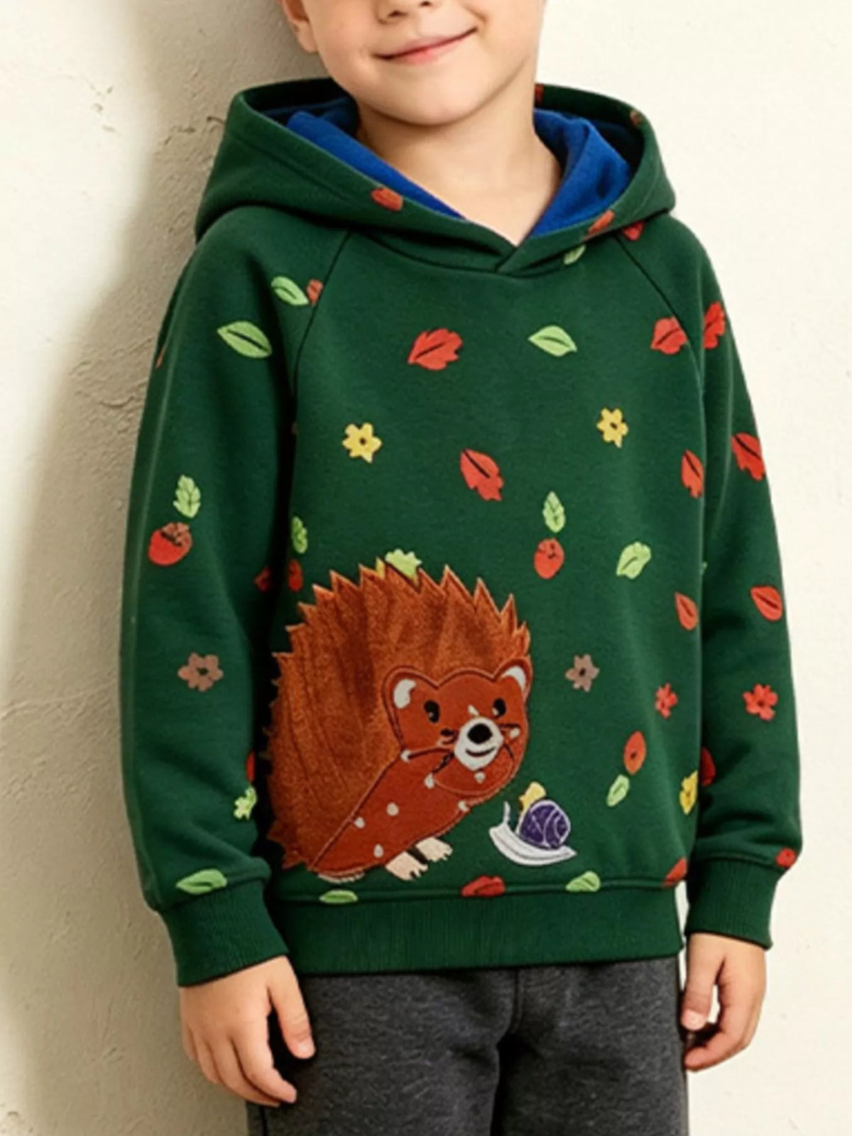 Children’s green hedgehog-print hoodie with contrasting blue hood lining worn by a child