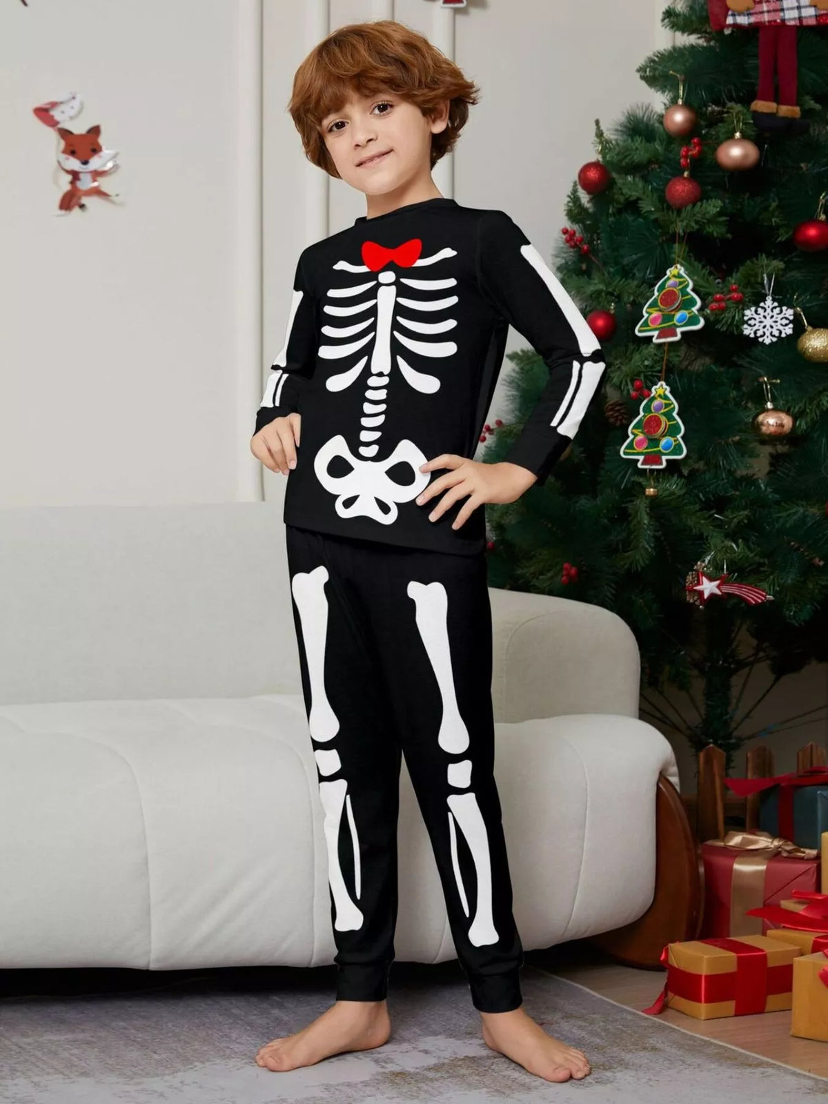 Child modeling black skeleton pajamas with a red bow graphic.