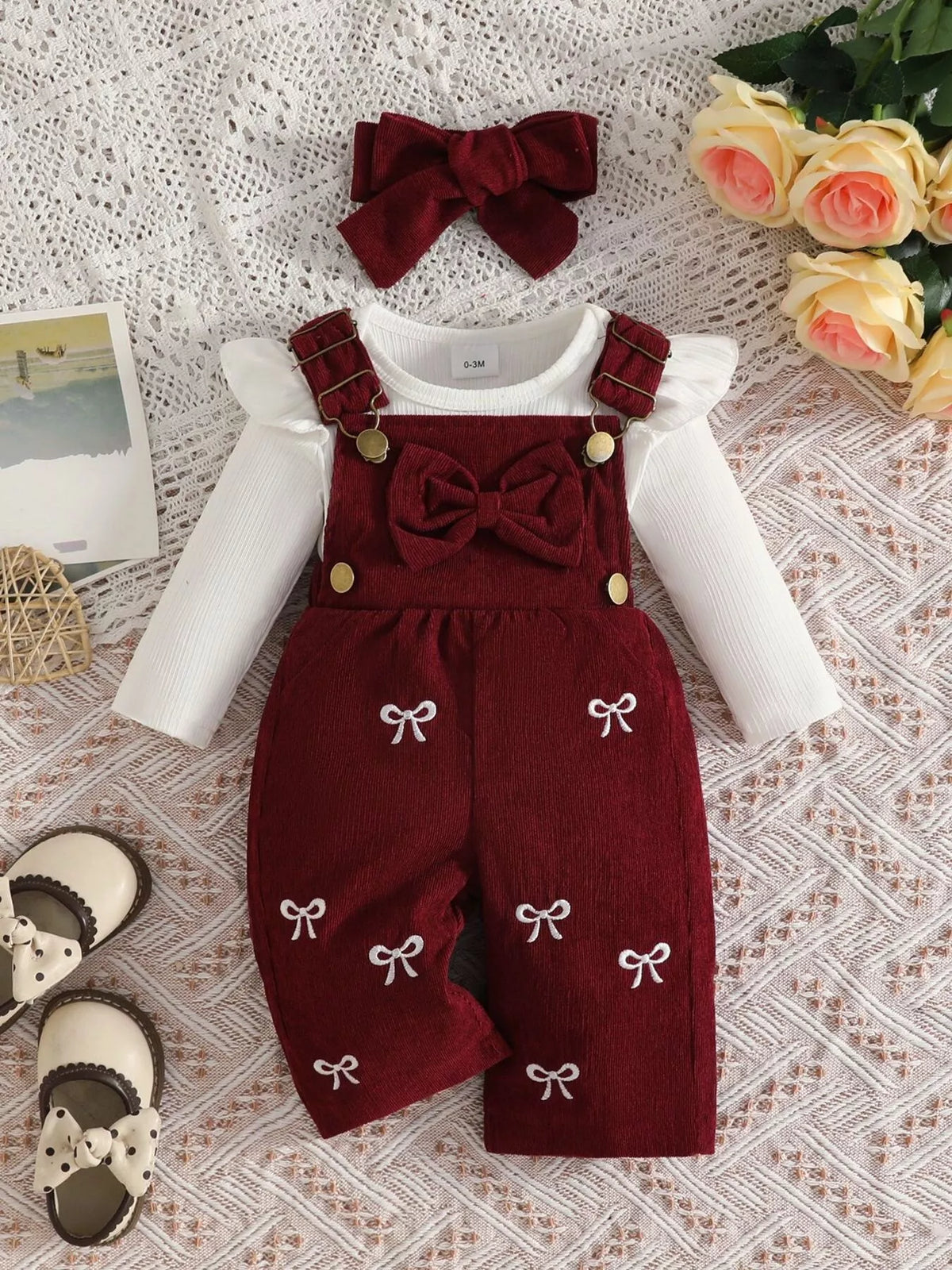 White ribbed baby bodysuit with burgundy bow-embroidered overalls and matching headband displayed flat