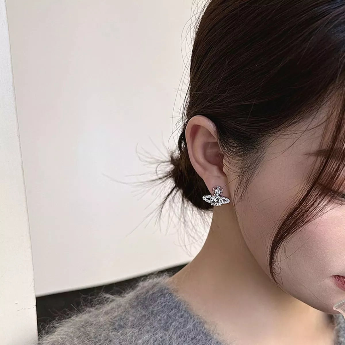 Silver-tone planet-shaped stud earrings with clear stones worn on a model