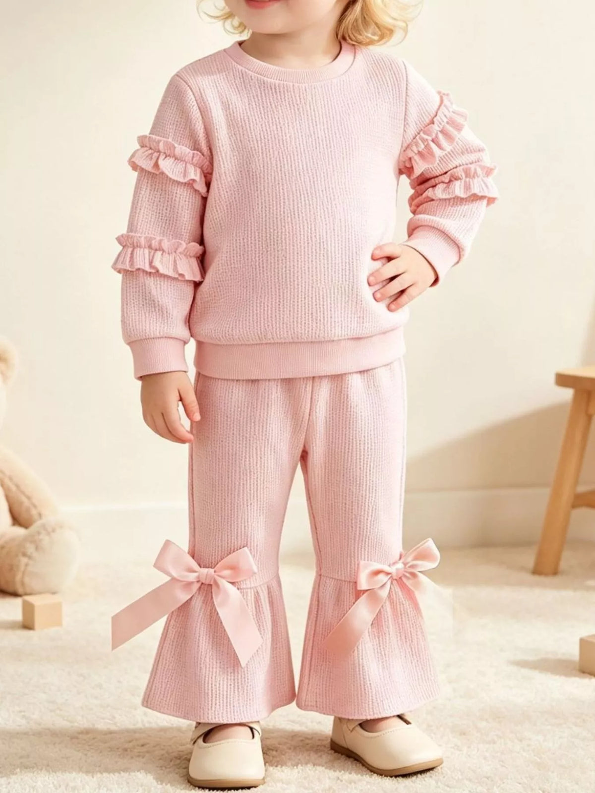 Pink ruffle-sleeve sweatshirt and bow-accented flared pants worn by a child