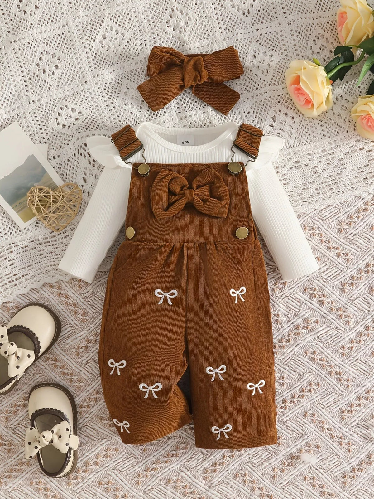 White ribbed baby bodysuit with brown bow-embroidered overalls and matching headband displayed flat