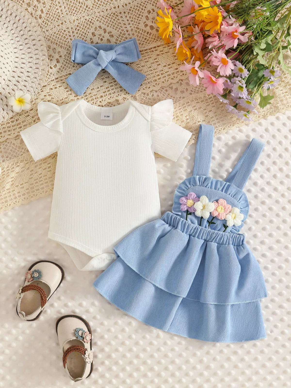 White bodysuit displayed beside the light blue flower-applique suspender skirt and bow headband.