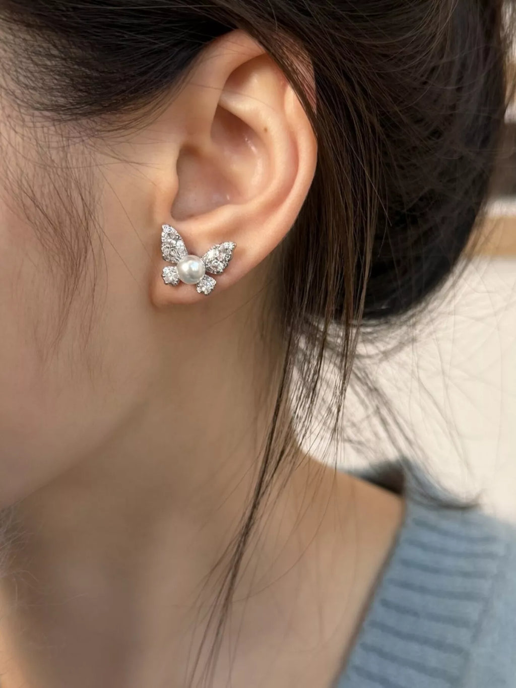 Butterfly-shaped pearl-like bead and clear stone stud earrings worn on a model