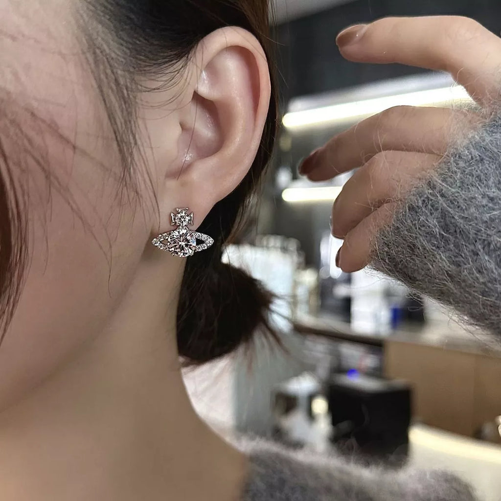 Silver-tone planet-shaped stud earrings with clear stones worn on a model