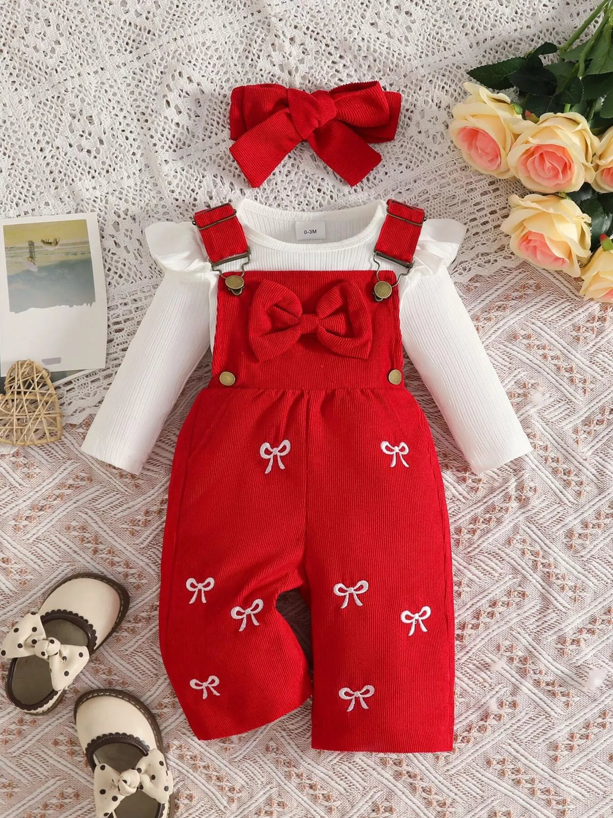 White ribbed baby bodysuit with red bow-embroidered overalls and matching headband displayed flat