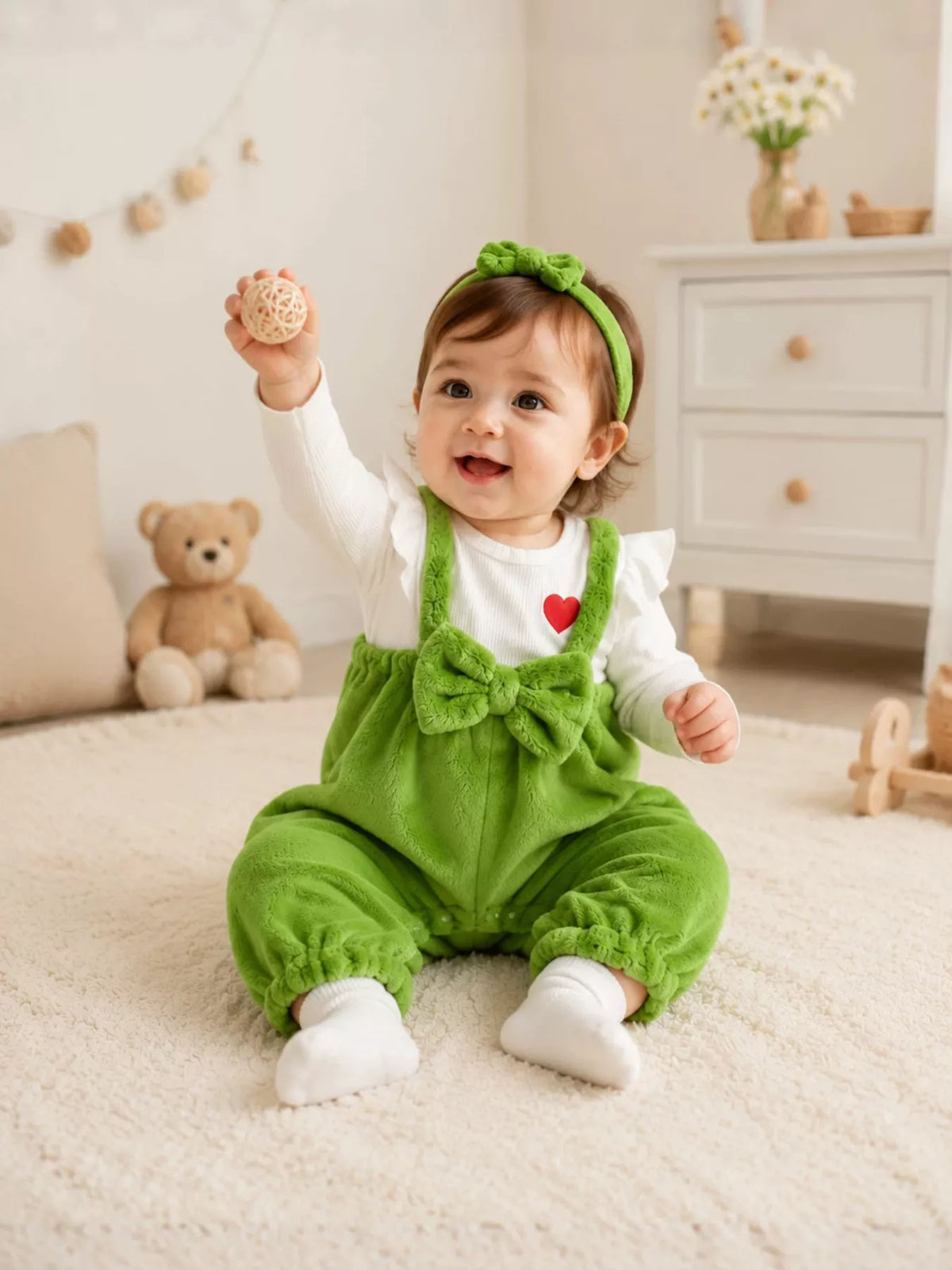 Green fuzzy baby overalls and matching bow headband with a white long-sleeve top worn by a baby