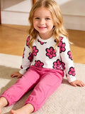 Seated child wearing a white pink-flower top and bright pink jogger pants.