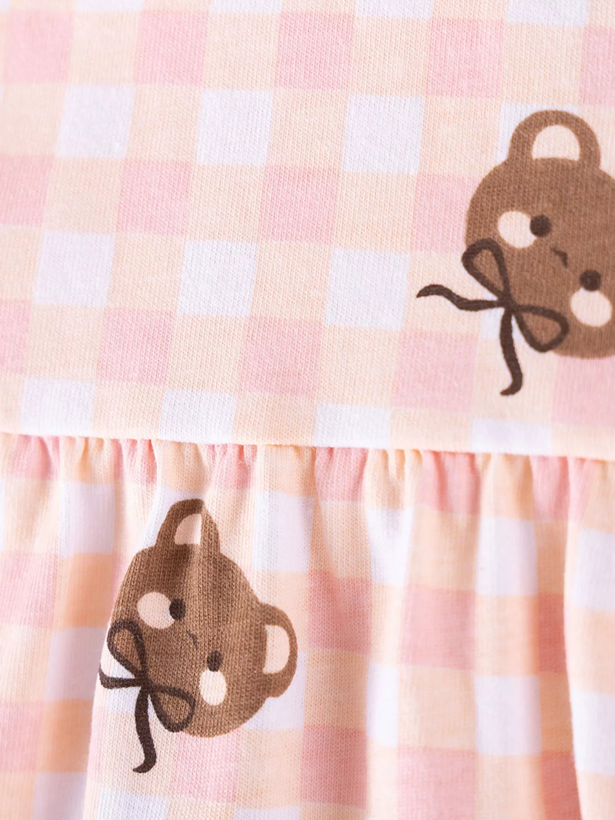 Close-up of the pink gingham bear print and gathered peplum seam.