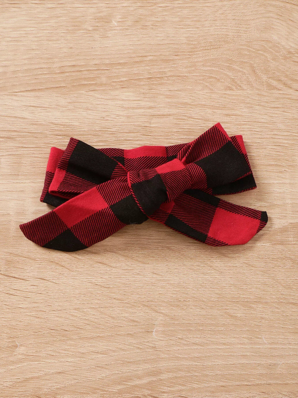 Red and black plaid bow headband on a wooden surface.