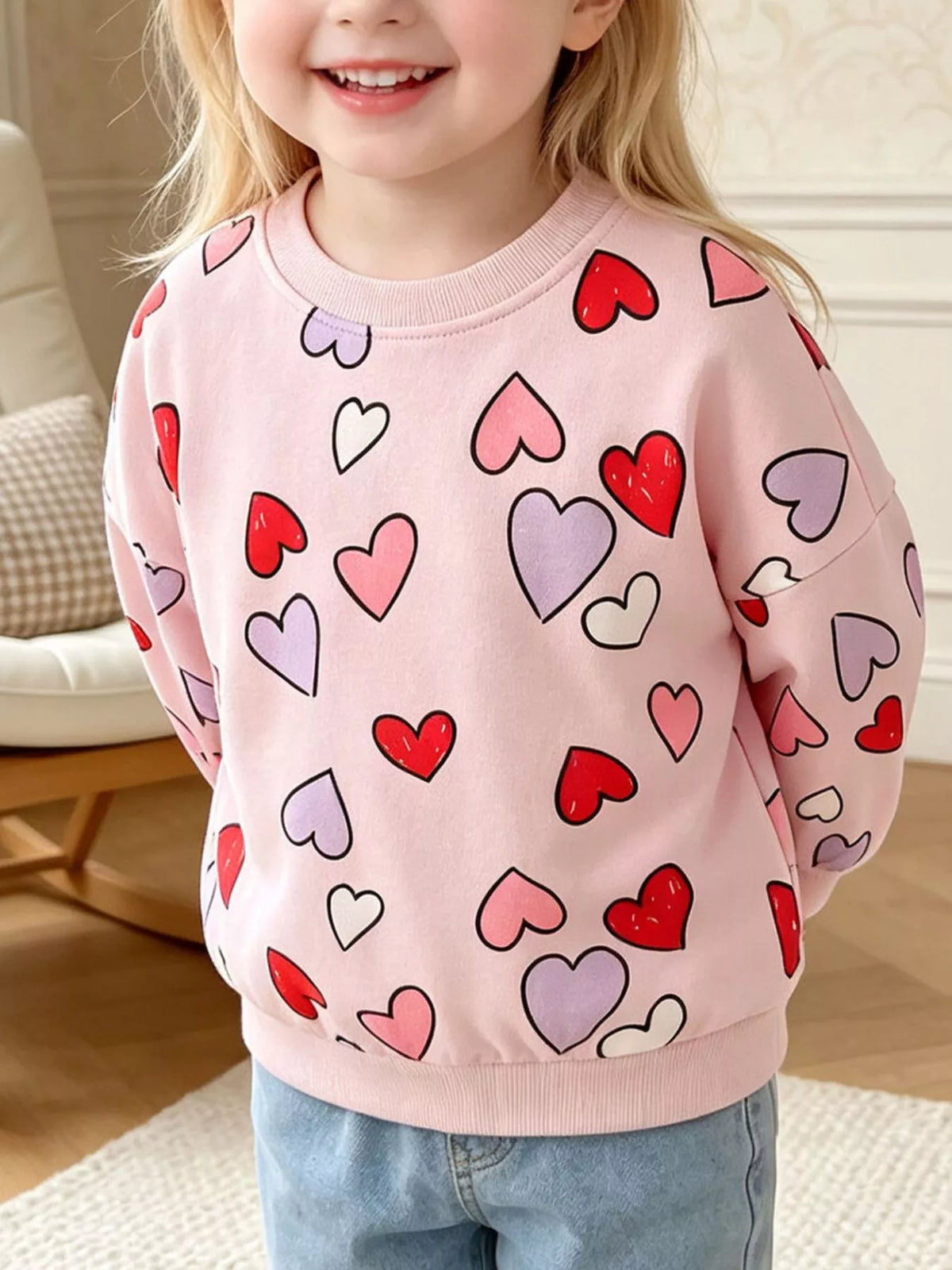 Children’s pink crewneck sweatshirt with red and white outlined heart print worn by a child