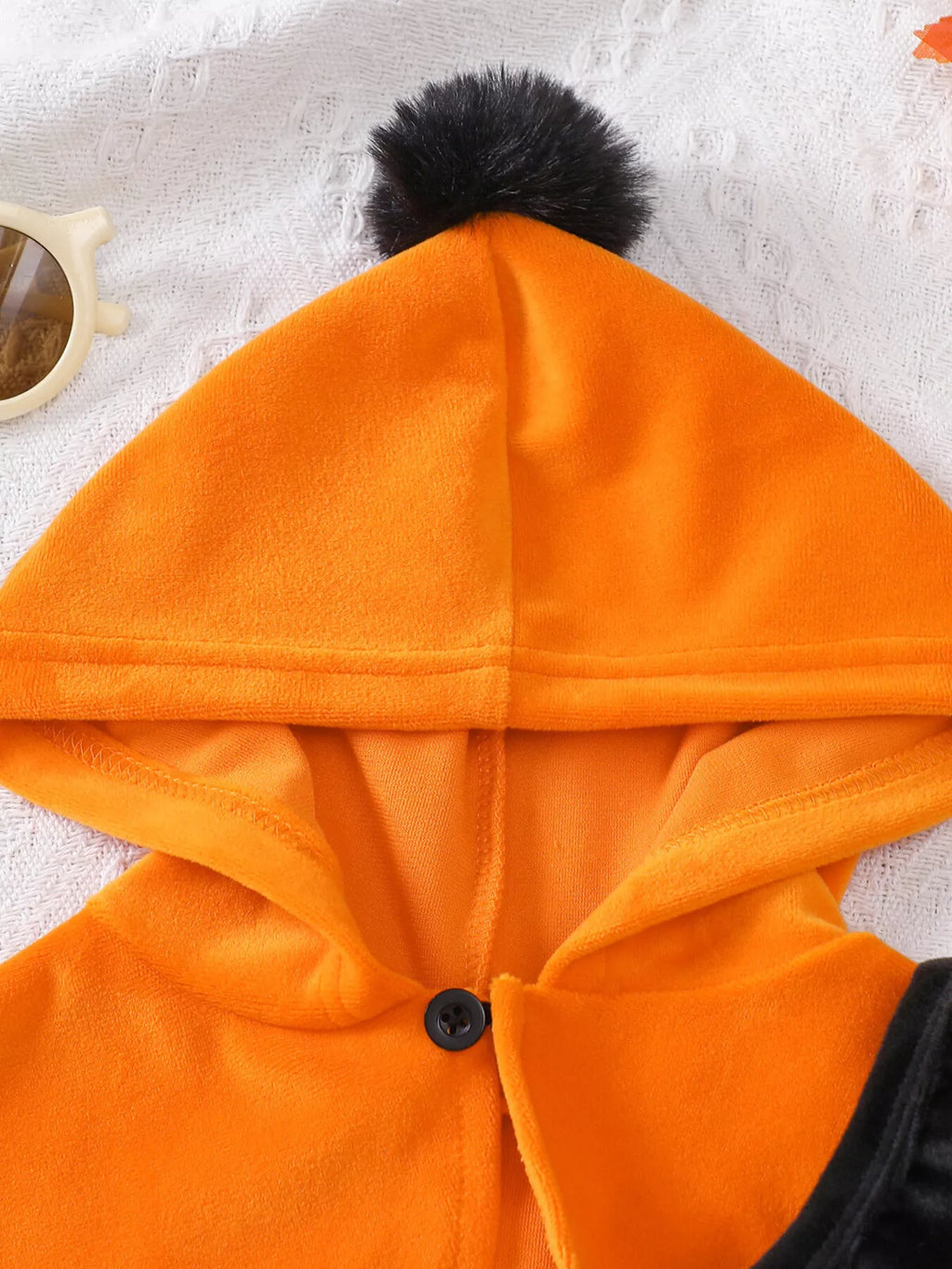 Close-up of the orange cape's hood and black pom-pom.