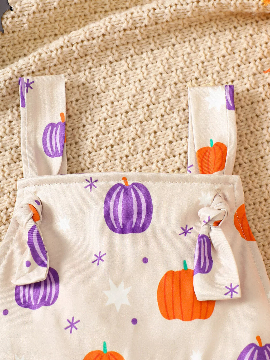 Close-up of the cream pumpkin-print overalls' shoulder straps and bib.