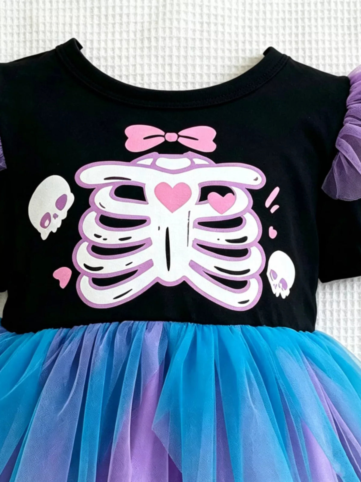 Close view of the white skeleton graphic, pink heart and bow on the black bodice.